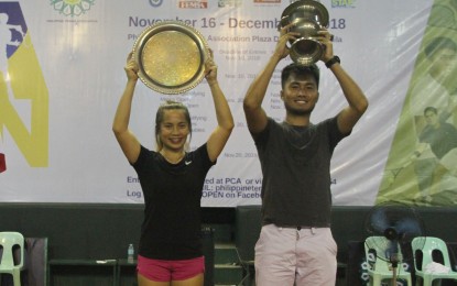 <p><strong>CHAMPIONS</strong>. Women's champion Marian Jade Capadocia and men's titlist Jeson Patrombon lift their trophies during the awarding ceremony of the 37th Philippine Columbian Association (PCA) Open Tennis Championships at the PCA indoor shell court in Paco, Manila on Sunday (Dec. 9, 2018).</p>