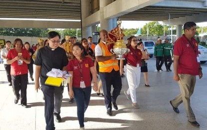 <p><strong>STO. NIÑO IN THE AIRPORT.</strong> GMR Cebu Airport Corporation chief executive advisor Andrew Harrison (center, wearing orange vest) carries the holy image of Señor Santo Niño de Cebu given by the Basilica Minore del Santo Niño, through its rector, Fr. Pacifico Nohara Jr. (in black clerical), to the Mactan Cebu International Airport, Jan. 14, 2019. <em>(Photo courtesy of Basilica Minore del Santo Niño Media Center/Analyn Conocono, USJ-R Communication Intern)</em>   </p>