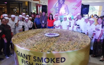 <p><strong>SMOKED FISH PIZZA. </strong>Mayor Susan Casareno and SM City Rosales Mall Manager Herald Eleria (middle) led the ceremonial torching and slicing of the giant smoked fish pizza showcasing the town's local product tinapa (smoked fish) as its main toppings. The giant pizza, which was assembled by students of SKD Academy last Saturday at the SM City Rosales event center, had a diameter of 10 feet and thickness of 10 centimeters that was later served to guests and mall goers.  <em>(Photo by Liwayway Yparraguirre)</em></p>