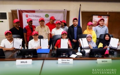 <p><strong>ADVANCING CHILDREN’S RIGHTS.</strong> Representatives from the Bangsamoro Autonomous Region in Muslim Mindanao (BARMM) led by Minister Naguib Sinarimbo (seated 2nd from left) of the Ministry of the Interior and Local Government – BARMM, among others, show the memorandum of agreement (MOA) they signed with Fanny Divino (center seated), senior program manager of Save the Children Philippines for Mindanao, during a ceremony held inside the BARMM compound in Cotabato City on Monday, July 1, 2019. <em><strong>(Photo courtesy of BPI-BARMM)</strong></em></p>