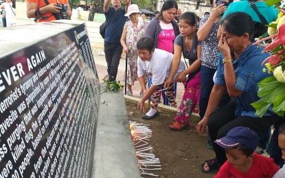 <p><strong>IN REMEMBRANCE.</strong> Family members of the victims of mass purging conducted by the New People's Army in Leyte in the '80s offer candles at a marker engraved with the names of over 100 victims. The survivors gathered during the 13th anniversary of the discovery of the victims’ remains at the plaza in Baybay City on Monday (Sept. 2, 2019). <em>(PNA photo by Sarwell Meniano)</em></p>