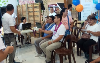 <p><strong>TRACING FAMILY.</strong> Digos City Vice Mayor Johari Baña (seated right) and The Church of Jesus Christ of Latter-Day Saints Digos stake (diocese) president, Atty. Nikkolo Marco Aurelio Cortes, (seated next to Baña) listens to Bing Concha (standing left) as he discusses ways on how to trace anyone's family tree up to the 6th generation using the Family Tree search app. Through the help of church volunteers, some residents managed to trace their lineage during the kick-off of the two-day Family Search Exhibit at the Second Floor of G-Mall in Digos City on Friday (September 28, 2019). <em>(PNA photo by Eldie S. Aguirre)</em></p>