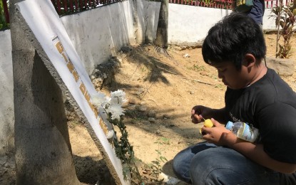 <p><strong>FLOWERS, CANDLE FOR GRANDMA.</strong> Ralph Ian Malabanan, 11, grandson of tabloid reporter and Ampatuan massacre victim Gina dela Cruz, lights a candle on a headstone bearing her grandmother’s name at the massacre site in Sitio Masalay, Barangay Salman in Ampatuan, Maguindanao during a visit last month. The promulgation of judgment against the accused is set on Thursday (Dec. 19). <em>(PNA photo by Allen V. Estabillo)</em></p>