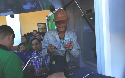 <p><strong>RICE FARMERS FINANCIAL AID</strong>. An elderly rice farmer (right) smiles as he withdraws the PHP5,000 unconditional cash transfer from the national government through the Department of Agriculture (DA) on Monday (Dec. 23, 2019) as DA Secretary William Dar (middle) looks on. The Rice Farmers Financial Assistance Program was launched in Pangasinan with 87,175 qualified rice farmer- beneficiaries. <em>(PNA photo by Hilda Austria)</em></p>