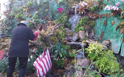 <p><strong>BAGUIO AND BENGUET MOUNTAINS</strong>. A landscaper places flowers and plants at the man-made small mountain at the Baguio City Hall Park that is replete with a waterfall and a well-decorated cave that will be one of the eight entries to the landscaping competition of the Baguio Flower Festival or the Panagbenga which will be launched on February 1. Some 13 landscapers, eight of them at the City Hall Park, four at the Lake Drive of Burnham and one at the Session Road Circle that once housed the stone sculpture of the eight commissioners of the second Philippine Commission will vie for the grand prize. <em>(PNA photo by Pigeon Lobien)</em></p>