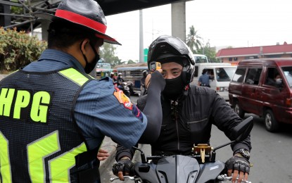 <p><strong>CHECKPOINT.</strong> An HPG personnel checks the temperature of a motorcycle rider at a checkpoint along the boundary of Cainta, Rizal and Marikina City during the early days of the enhanced community quarantine in March. Presidential Spokesperson Harry Roque raised the possibility that the IATF might downgrade the classification of community quarantine in places under MGCQ and general community quarantine. <em>(File photo)</em></p>