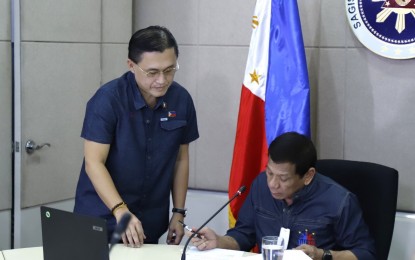 <p><strong>ADDITIONAL POWERS</strong>. Senator Bong Go assists President Rodrigo Duterte as the Chief Executive signs Republic Act 11469 or Bayanihan to Heal as One Act on Tuesday (March 24, 2020). The new law grants Duterte additional powers to implement measures to fight the coronavirus spread. <em>(Contributed photo)</em></p>