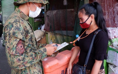 <p><strong>CHECKPOINT</strong>. A police personnel checks a woman's quarantine pass at the Cloverleaf Market in Balintawak, Quezon City on April 15, 2020. Authorities are implementing stricter rules to curb the spread of the coronavirus disease 2019 (Covid-19). (<em>PNA photo by Robert Oswald P. Alfiler</em>)</p>