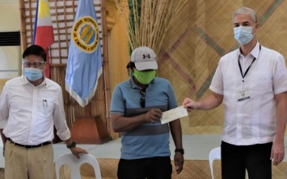 <p><strong>ASSISTANCE</strong>. A former rebel in Negros Occidental receives a check worth PHP15,000 as immediate assistance from Governor Eugenio Jose Lacson (right), in the presence of Department of the Interior and Local Government Provincial Director Ferdinand Panes in rites at the Capitol Social Hall in Bacolod City on Thursday (July 16, 2020). The cash benefit is provided under the government’s Enhanced Comprehensive Local Integration Program or E-CLIP. <em>(Photo courtesy of PIO Negros Occidental)</em></p>