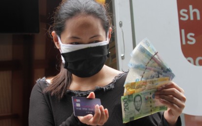 <p><strong>MOBILE 'PARAÑACASH'.</strong> A beneficiary of the Parañaque City government's financial assistance program shows her cash withdrawn through Union Bank's Mobile Parañacash ATM during its launch in Barangay San Agustin on Wednesday (Aug. 5, 2020). Some 55,000 beneficiaries received the second tranche of the city government's financial assistance through the mobile ATM project. <em>(PNA photo by Avito C. Dalan)</em></p>