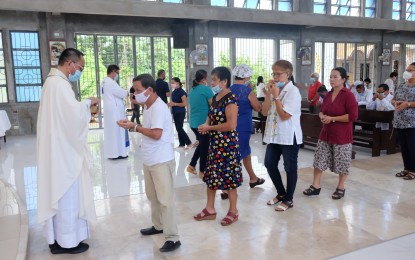 <p><strong>HOLY COMMUNION</strong>. Fr. Ronnie Ablong (left), one of two exorcists of the Diocese of Dumaguete, gives communion during a Holy Mass at his recent installation being the new priest-in-charge of the St. Vincent Ferrer quasi-parish in Dumaguete City. The priest recommends a prayerful life and receiving the sacraments to ward off diabolical attacks during this time of a pandemic. <em>(Photo by Judy Flores Partlow)</em></p>