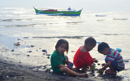 <p><strong>COASTAL VILLAGE</strong>. Children play on the shore in the coastal barangay of Macabalan, Cagayan de Oro City, as a fishing boat floats idly nearby. The Region 10 office of the Bureau of Fisheries and Aquatic Resources is located in this coastal barangay. <em>(Photo by Jigger J. Jerusalem)</em></p>