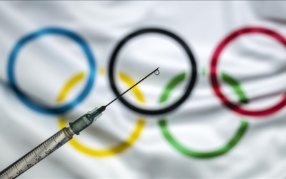 <p>In this photo illustration taken in Ankara, Turkey on Dec. 30, 2020 a vaccine syringe with a drop on the needle's end is seen in front of a computer screen showing the flag of International Olympic Committee (IOC). <em>(Ali Balıkçı - Anadolu Agency)</em></p>