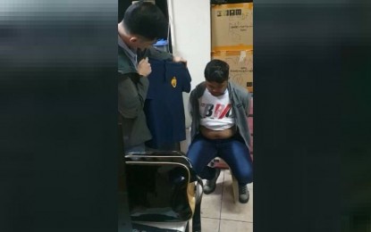 <p><strong>NABBED.</strong> An NBI agent takes a look at the polo shirt used by suspect Mark Cabal (right) who was arrested in an entrapment at the NBI headquarters in Manila on Feb. 3, 2021. Cabal was arrested for posing as an employee of the bureau and extorting money from a clearance applicant.<em> (Photo courtesy of NBI)</em></p>