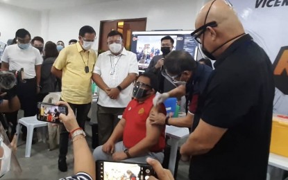 <p><strong>FIRST VACCINEE IN VISAYAS</strong>. Chief of the Vicente Sotto Memorial Medical Center, Dr. Gerardo Aquino Jr. (in red), receives his first dose of the China-made CoronaVac from Health Undersecretary Gerardo Bayugo during the ceremonial rollout of the national vaccination campaign in Cebu City on Thursday (March 4, 2021), as Presidential Spokesperson Harry Roque (3rd from left), IATF deputy chief implementer Melquiades Feliciano (right) and Cebu City Vice Mayor Michael Rama (2nd from left) look on. Aquino was the first medical front-liner in the Visayas and Mindanao to receive the vaccine. <em>(PNA photo by John Rey Saavedra)</em></p>