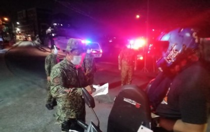 <p><strong>CURFEW VIOLATORS.</strong> A police officer checks on a motorcycle rider at a checkpoint on Monday (March 15, 2021). Police officers have arrested a total of 1,449 violators on the first day of the reimplementation of unified curfew hours from 10 p.m. to 5 a.m. in Metro Manila. <em>(Photo courtesy of PNP)</em></p>