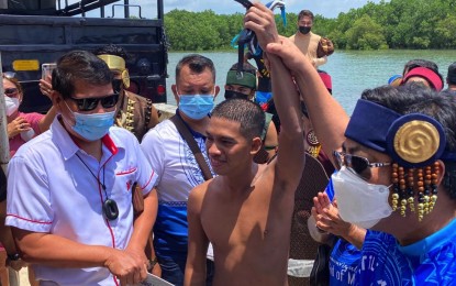 <p><strong>HISTORIC FULL SWIM</strong>. Mayor Junard Chan (right) raises the hand of Cleevan Alegres, 25, dubbed as the "Little Merman" of Cebu. The open-water swimmer completed his circumnavigation of Mactan Island shortly before noon Monday (April 26, 2021).<em> (Photo courtesy of Mayor Junard Chan)</em></p>