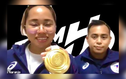 <p><strong>SHE DID IT.</strong> Hidilyn Diaz shows her Tokyo 2020 gold medal with her coach Julius Naranjo during a virtual meeting with the Philippine Embassy in Japan on Tuesday (July 27, 2021). Diaz made history by ending the Philippines' almost a century-old gold medal quest that began in the Paris 1924 Olympics and setting a record for the women’s 55 kilograms category. <em>(Photo courtesy of Philippine Embassy - Tokyo)</em></p>