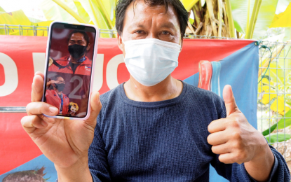 <p><strong>PROUD FOSTER PARENT</strong>. Ahmad Janius Abdullah holds a phone with photos of Olympics gold medalist Hidilyn Diaz at his home in Kampung Kesang Tua, Melaka on July 27, 2021. Ahmad Janius, deputy president of the Malaysian Weightlifting Federation (MWF), served as Hidilyn’s foster parent during her more than one year training in Malaysia before the Olympics. <em>(Photo courtesy of Bernama)</em></p>