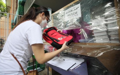 <p><strong>FREEBIES.</strong> A mother claims her child’s free school supplies at the Taguig Integrated School in Barangay Sta Ana on Monday (Sept. 13, 2021), the first day of Academic Year 2021-2022 for public school students. The package includes a bag, pair of shoes, raincoats, modules, and emergency kits. <em>(PNA photo by Avito Dalan)</em></p>
