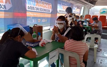 <p><strong>MOBILE VACCINATION.</strong> A Red Cross volunteer (seated right) prepares to administer the coronavirus disease 2019 (Covid-19) vaccine to a resident of General Santos City during the first stop of the mobile vaccination program last Saturday at the city’s main public market in Barangay Dadiangas South. The city government deployed a converted “bakuna bus” for the vaccination activity. <em>(Photo courtesy of the city government)</em></p>