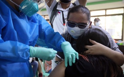 <p><strong>PROTECTION.</strong> A young vaccinee is comforted by her guardian as she receives her Covid-19 jab in Las Piñas on Friday (Oct. 22, 2021). The vaccination included adolescents aged 12 to 17, following the initial rollout for the 15-17 age group one week ago. <em>(PNA photo by Avito Dalan)</em></p>
