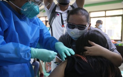 <p><strong>PROTECTION</strong>. A young vaccinee is comforted by her guardian as she receives her Covid-19 jab in Las Piñas on Friday (Oct. 22, 2021). The average daily jabs administered in the last seven days stood at 454,764 doses. <em>(PNA photo by Avito Dalan)</em></p>