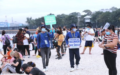 <p><strong>GENTLE REMINDER.</strong> Two marshals hold a placard  reminding visitors at the Manila Baywalk Dolomite Beach to observe minimum health protocols on Monday (Oct. 25, 2021). The Manila Police District has been tasked to deploy more police personnel to ensure crowd control in the area, which draws a lot of visitors, especially during weekends. <em>(PNA photo by Joey O. Razon)</em></p>