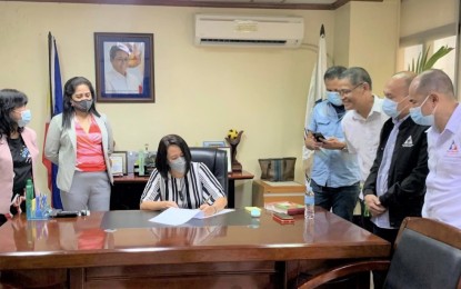 <p><strong>DIGITIZATION</strong>. Lawyer Marion Sevilla (seated), newly assumed DOLE-7 officer in charge, signs a document while other labor officials look on. Sevilla on Friday (Dec. 3, 2021) said the agency is eyeing adopting digital transactions to limit physical interactions and ensure the well-being of the employees and transacting public amid the Covid-19 crisis. <em>(Photo courtesy of DOLE-7)</em></p>