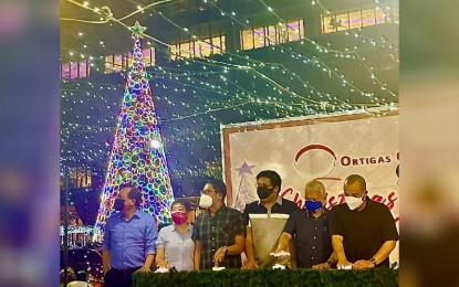<p><strong>UNITY XMAS TREE.</strong> Mayor Vico Sotto’s representative, Pasig City Administrator Jeronimo Manzanero (extreme right), and Barangay San Antonio chairman Raymond Lising (3rd from left) lead the ceremonial lighting of the 30-feet “Twin Christmas Trees” (2nd Xmas tree hidden) at the Ortigas Business District in Pasig City on Dec. 1, 2021. There are two Christmas Trees at the intersection of J. Vargas and San Miguel Avenues to symbolize the unity among businesses in the area as they help each other to cope with the effects of the health crisis. <em>(Photo courtesy of Barangay San Antonio, Pasig City)</em></p>