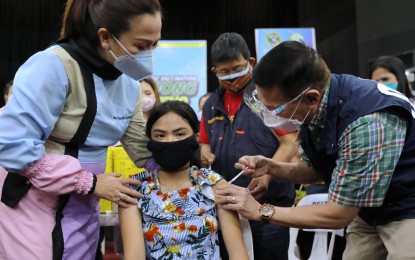 <p><strong>JABS FOR TEENS</strong>. Health Secretary Francisco T. Duque III (right) administers a Covid-19 vaccine to a teenage girl during the extended "Bayanihan, Bakunahan" vaccination drive at the De La Salle University campus in Dasmariñas, Cavite on Dec. 3, 2021. The Philippines has now administered a total of 91,777,433 doses of coronavirus vaccine nationwide.<em> (PNA photo by Joey O. Razon)</em></p>