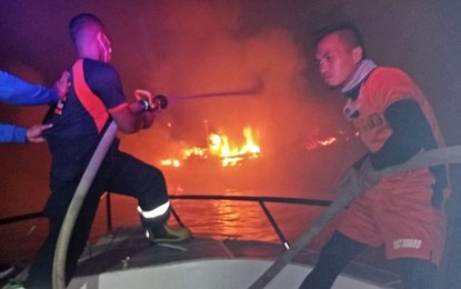 <p><strong>VESSEL ON FIRE.</strong> A fireman, assisted by a Philippine Coast Guard personnel, tries to put out the blaze as a wooden-hulled vessel catches fire around 2:20 a.m. Tuesday (Dec. 7, 2021) off Lampinigan Island, Isabela City, Basilan province. Some PHP13.5 million worth of properties went up in smoke.<em> (Photo courtesy of CGSS-Isabela City)</em></p>