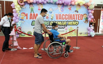 <p><strong>VAX FOR SENIORS.</strong> Eligio Reyes, 69, from Barangay Salawag (on wheelchair), a person with disability (PWD), is assisted by his son after receiving a second dose Covid-19 vaccine shot at the Ugnayang La Salle Gymnasium in Dasmariñas City, Cavite on Feb, 17, 2022. The national government has been encouraging local government units to consider house-to-house vaccination drives to inoculate senior citizens and persons with comorbidities who are unable to go to vaccination sites. <em>(PNA photo by Gil Calinga)</em></p>
