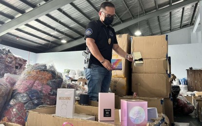 <p><strong>SEIZED.</strong> Customs Intelligence Officer 3 Alvin Enciso inspects the seized PHP250 million worth of fake luxury items in Las Piñas City during a raid on Friday (April 22, 2022). Counterfeit apparel and bottles of perfume were confiscated. <em>(Contributed photo)</em></p>