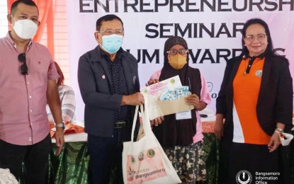 <p><strong>CASH AID.</strong> A widow of war from Maguindanao receives livelihood aid of PHP20,000, certificates for livelihood training, and tokens from Bangsamoro Autonomous Region in Muslim Mindanao (BARMM) lawmaker Susana Anayatin (right) and BARMM Minister of Trade, Investment, and Tourism Abuamri Taddik (2nd from left). The aid provided Monday (July 11, 2022) to at least 50 widows is part of government assistance to the vulnerable sector in the region.<em> (Photo courtesy of MTIT)</em></p>