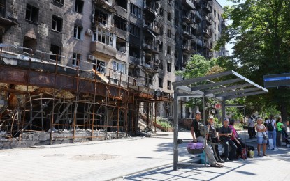 <p>Local residents wait for the bus near damaged city buildings in Mariupol on July 15, 2022. <em>(Photo by Victor/Xinhua)</em></p>