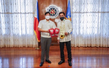 <p><strong>CHAMP.</strong> President Ferdinand Marcos Jr. (left) receives a pair of boxing gloves from new world champion Dave Apolinario at Malacañang Palace on Aug. 3, 2022. Apolinario is the new International Boxing Organization flyweight king after a first-round knockout of Gideon Buthelezi at the South African’s turf on July 29. <em>(Photo courtesy of BBM Facebook)</em></p>