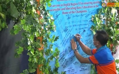 <p><strong>COMMITMENT</strong>. A personnel from the Department of Education signs at the wall of commitment to support the programs and advocacy of the department during the regional launching of the Brigada Eskwela held at the Capiz Villareal Stadium on Monday (Aug. 8, 2022). This year’s Brigada is geared towards preparing for the face-to-face classes in November. <em>(Screenshot from DepEd livestreaming) </em></p>