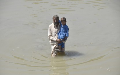 <p>A man with a child wades through flooded water in northwest Pakistan's Charsadda on Aug. 31, 2022. <em>(Photo by Saeed Ahmad/Xinhua)</em></p>