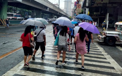 <p>Commuters shield themselves from the rain using umbrella as they walk along a crosswalk on Pedro Gil Street in Manila. <em>(PNA photo by Alfred Frias)</em></p>