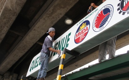 <p><strong>EQUAL TREATMENT.</strong> Workers fix a signage of the Metro Manila Development Authority and Department of Transportation along Quezon Avenue in Quezon City in this October 2022 photo. Senators are seeking a 13th-month bonus for all government workers, regardless of employment status. <em>(PNA photo by Jess M. Escaros Jr.) </em></p>