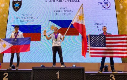 <p><strong>CHAMPION:</strong> Kahlil Adrian Viray (center) waves the Philippine flag during the awarding ceremony of the Standard Overall event at the 19th International Practical Shooting Confederation (IPSC) Handgun World Championships in Pattaya, Thailand on Dec. 3, 2022. With him on the podium are teammate and silver medalist Rolly Nathaniel Tecson (left) and bronze medalist Nils Jonasson from the United States. <em>(Contributed photo)</em></p>