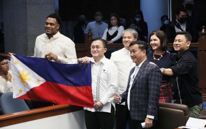 <p><strong>GILAS ASSET</strong>. Barangay Ginebra import Justin Brownlee (left) holds the Philippine flag as he poses with members of the Philippines Senate who approved a bill granting him Filipino citizenship on Dec. 12, 2022. Once signed into law by President Ferdinand R. Marcos Jr., Brownlee will qualify to play for Gilas Pilipinas in the February window of the FIBA World Cup Qualifiers. <em>(File photo)</em></p>
