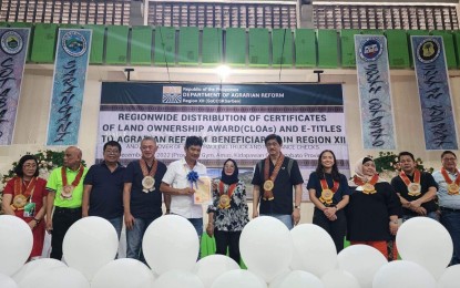 <p><strong>PROUD LANDOWNER.</strong> Ruben Rivas (center, in white), a farmer beneficiary from Columbio Sultan Kudarat, shows the certificate of land ownership award (CLOA) he received from Department of Agrarian Reform (DAR) Secretary Conrado Estrella (5th from right) on Dec. 10, 2022 in Kidapawan City. At least 3,524 beneficiaries benefited from the DAR CLOA distribution in the Soccsksargen Region covering the provinces of South Cotabato, North Cotabato, Sultan Kudarat and Sarangani. <em>(Photo courtesy of DAR)</em></p>