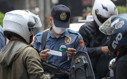 <p><strong>CHECKPOINT.</strong> A member of the Manila Police District Station 14 in Quiapo, Manila checks the driver's license of motorists passing along Claro M. Recto Avenue in this December 2022 photo. The police enhance crime prevention by beefing up visibility. <em>(PNA photo by Yancy Lim)</em></p>
