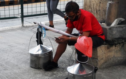<p><strong>NO EXEMPTION.</strong> A vendor of native snacks scans his mobile phone while waiting for buyers at the foot of the Metro Rail Transit-3 station in Barangay Guadalupe, Makati City in this undated photo. Under a new law, all existing users should register their subscriber identity module cards or face deactivation. <em>(PNA photo by Jess M. Escaros Jr.)</em></p>