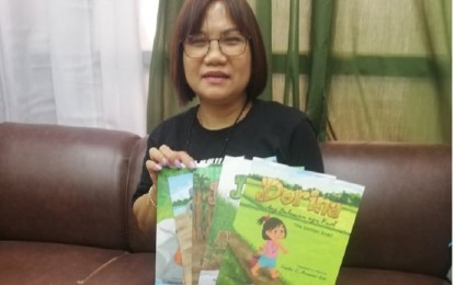 <p><strong>EXHIBIT</strong>. Kinaray-a book writer Linda Lee (center) holds a copy of her book that forms part of her exhibit at the Iloilo Museum of Contemporary Art in Iloilo City on Jan. 3, 2023. Lee calls for more writers to write children's books in Kinaray-a, local language of Antique province.<em> (PNA photo by AJPetinglay)</em></p>