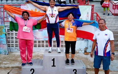 <p><strong>GOLD MEDALIST</strong>. Javelin legend Erlinda Lavandia (center) holds the Philippine flag during the awarding ceremony at the Kuala Lumpur International Masters Athletics Championships in Malaysia on Dec. 4, 2022. At far right is National Masters Seniors Athletic Association of the Philippines (NMSAAP) President Jose Ang Jr.<em> (Contributed photo)</em></p>