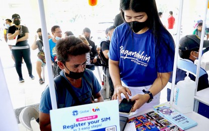 <p><strong>COMPLIANCE.</strong> A staff member of a telecommunications company (standing) assists a client in registering his subscriber identity module card at a stall at the Quezon City Hall grounds on Tuesday (Jan. 24, 2023). Republic Act 11934 or the SIM Card Registration law seeks to put an end to scams and gives subscribers until April 26 to register if they want to keep their numbers active.<em> (PNA photo by Ben Briones)</em></p>