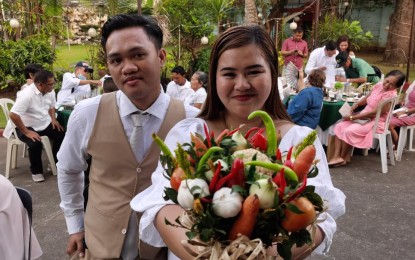 <p><strong>PRACTICAL BOUQUET</strong>. Newlywed couple Paul John Tagle and Danica Dalmacia are shown at the mass wedding ceremony in Cavite City on Monday (Feb. 13, 2023). The bride's bouquet is made up of mixed vegetables, including the pricey onions.<em> (PNA photo by Rossel Calderon)</em><br /><br /></p>